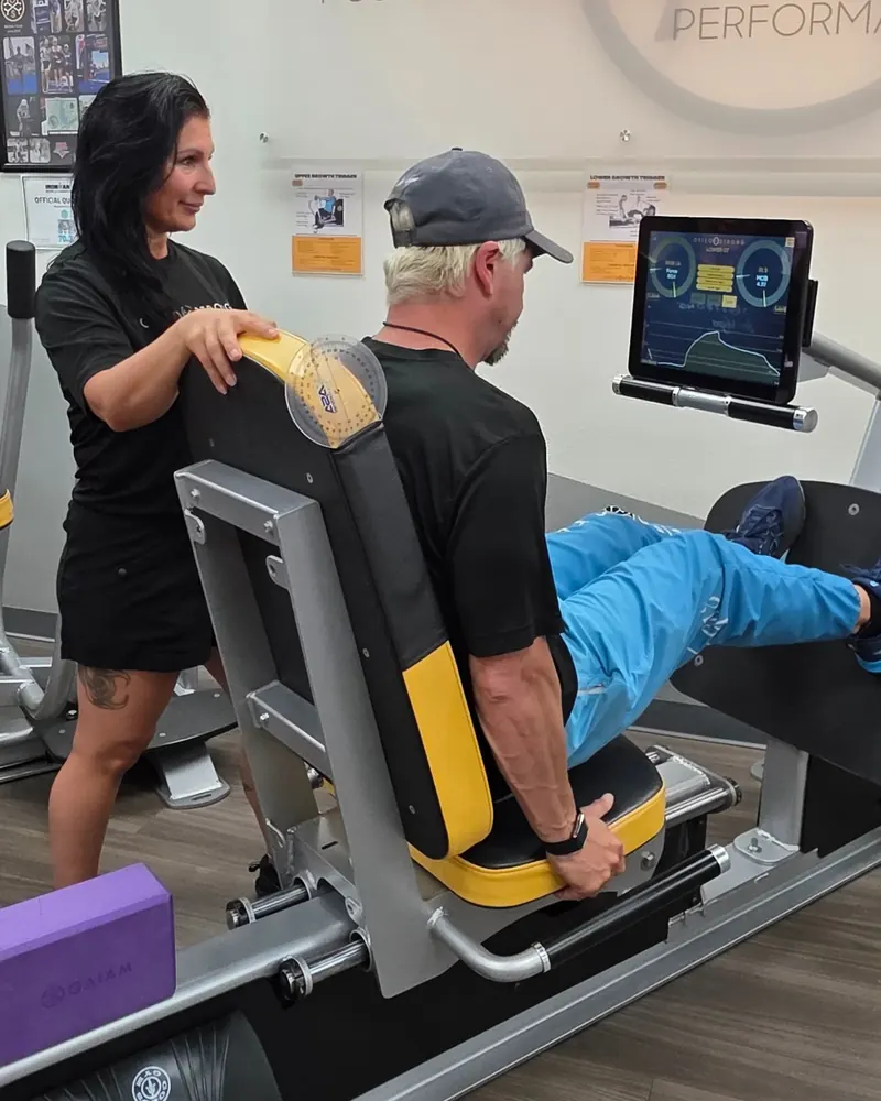 A member pushes with his feet on the lower body station as a coach watches, the force curve on the screen